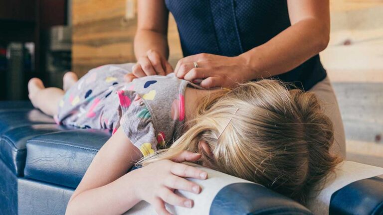 Adult sitting on a couch performing a gentle neck stretch with one hand on the side of the head.